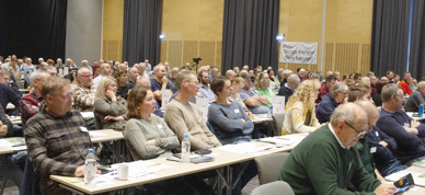 Delegater fra organisasjonen sitter på rekke og rad under landsmøtet. Alle ser fremover mot scenen. I bakgrunnen henger et banner hvor det står "Norge trenger flere bønder" - Foto: Nora May Engeseth/NBS